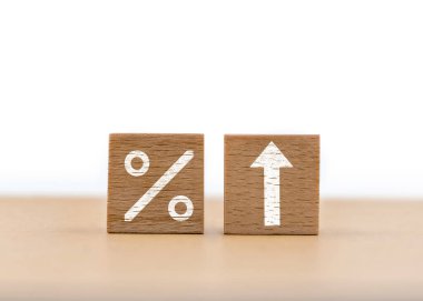 İki tahta blok bir masada oturuyor, biri yüzde işareti gösteriyor, diğeri ise yukarı doğru ok atıyor, büyüme ve mali ilerleme kavramını aktarıyor..