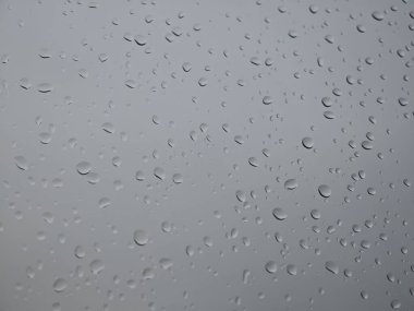 Pencere camındaki yağmur damlaları dışarıdaki manzarayı bozuyor. Tepemizde gri bulutlar beliriyor, yağmurlu günün sakin atmosferini artırıyor.