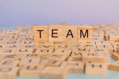 Scrabble kiremitleri kelime takımını diğer harf kiremitleriyle dolu bir masanın üstünde gösterir. Ayarlar, harflerin doğal ışık altında eğlenceli bir düzenlenmesini gösteriyor.