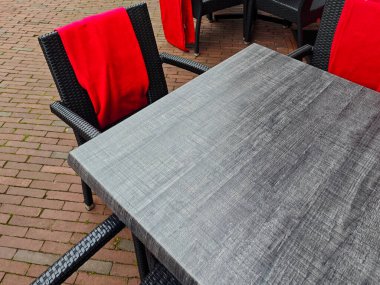 Koyu ahşaptan yapılmış şık bir açık hava yemek masası iki hasır sandalyeyle kurulur. Sandalyelerin üzerinde parlak kırmızı battaniyeler asılı, davetkar atmosfere biraz sıcaklık katıyor.