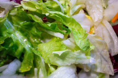 Yeşil renk ve dokuları gösteren çeşitli yapraklı taze marul yakın çekim. Sahne, doğal ışığın marulu aydınlattığı bir mutfakta geçiyor..