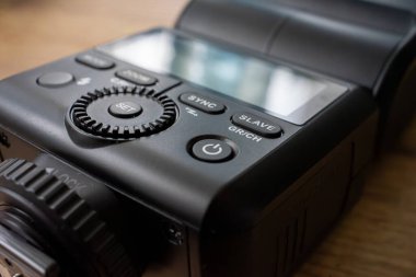 Bir kamera flaş cihazı ahşap bir yüzeye yerleştirilir. Flaş ayarlarını kontrol eden düğmeleri kapat. Cihaz bir fotoğraf oturumunda veya stüdyo ortamında kullanılmaya hazırdır