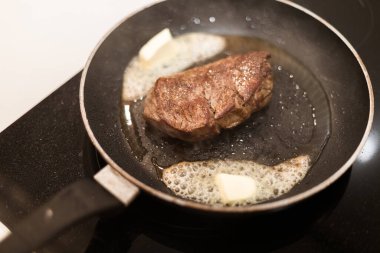 Biberiyeli ve tereyağlı tavada biftek pişirme süreci.