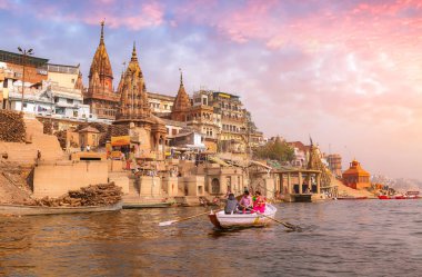 Varanasi şehir mimarisi gün batımında turistle Ganj nehrinde tekne gezintisinin keyfini çıkarırken