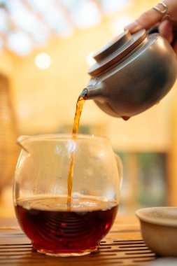 Geleneksel Çay Seremonisi Clay Teapot 'un yakın planından dökülüyor. Geleneksel bir çay seremonisi sırasında sıcak çayın kil çaydanlıktan küçük bir fincana nazikçe döküldüğü yakın çekim görüntüsü. Kültür, sağlık ve mutfak temaları için mükemmel..