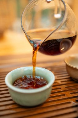 Sıcak çay demlikten fincana dökülür, geleneksel tören, yakın çekim. Geleneksel bir ortamda sıcak çay dökme anı. Taze demlenmiş çaydanlık ve fincanı birbirine bağlayan odaklanmış çay, ayin ve ferahlatıcılığı sembolize eder..