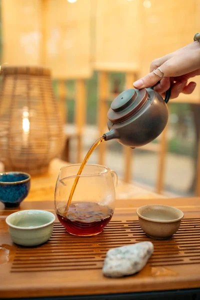 Sıcak çay demlikten fincana dökülür, geleneksel tören, yakın çekim. Geleneksel bir ortamda sıcak çay dökme anı. Taze demlenmiş çaydanlık ve fincanı birbirine bağlayan odaklanmış çay, ayin ve ferahlatıcılığı sembolize eder..