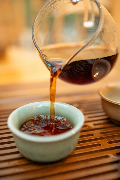 Sıcak çay demlikten fincana dökülür, geleneksel tören, yakın çekim. Geleneksel bir ortamda sıcak çay dökme anı. Taze demlenmiş çaydanlık ve fincanı birbirine bağlayan odaklanmış çay, ayin ve ferahlatıcılığı sembolize eder..