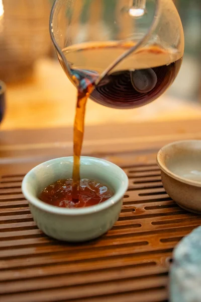 Sıcak çay demlikten fincana dökülür, geleneksel tören, yakın çekim. Geleneksel bir ortamda sıcak çay dökme anı. Taze demlenmiş çaydanlık ve fincanı birbirine bağlayan odaklanmış çay, ayin ve ferahlatıcılığı sembolize eder..