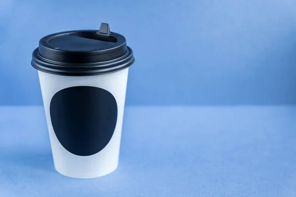 white paper kraft disposable cup for coffee with black plastic lid. coffe to go on blue background.