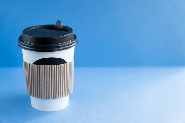 white paper kraft disposable cup for coffee with black plastic lid. coffe to go on blue background.
