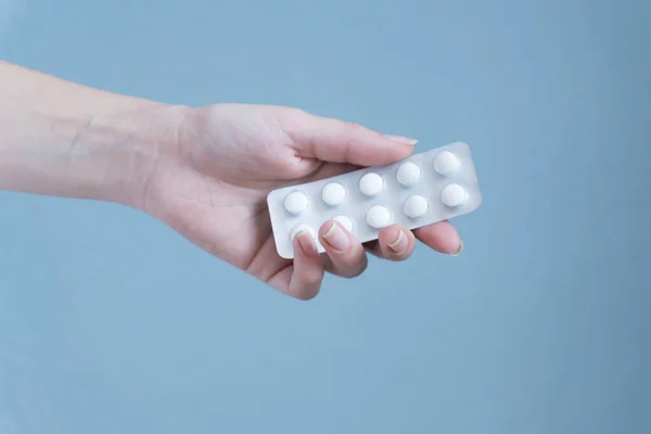 Woman hand holding blister of pills on blue background.