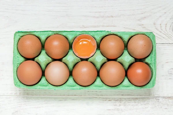 top view of green carton egg box full of raw fresh brown chicken eggs and egg yolk on wooden background