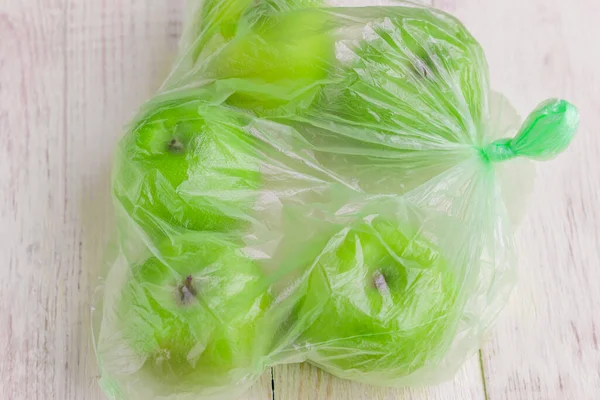 Fresh green apples in plastic bag on wooden table. environmental concept of non-ecological use of plastic