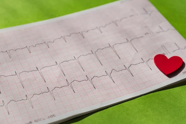 close up of an electrocardiogram in paper form vith red wooden heart. ECG or EKG paper on green  background.  medical and healthcare concept.