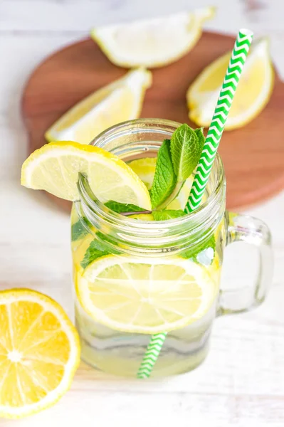 Mason jar glass of homemade lemonade with lemons, mint and green paper straw on wooden rustic background. Summer refreshing beverage.