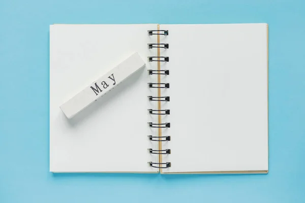 Clean spiral note book for notes and messages and may wooden calendar bar on blue background. Minimal business flat lay