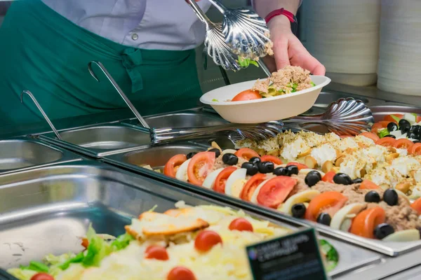 buffet self-service food display human hand take plate and put a salad. full lunch service station