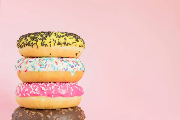 Stack of glazed sweet doughnuts with sprinkles and nuts on pink background. Copy pace for your text