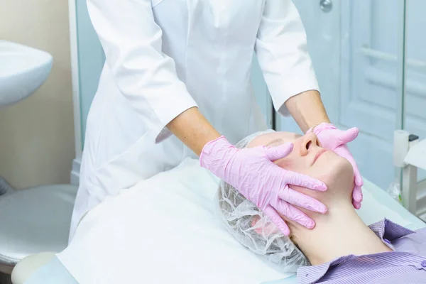 Beautician in pink gloves applies peeling on woman face. Cosmetic procedure for rejuvenation and cleansing of the skin. Spa treatment