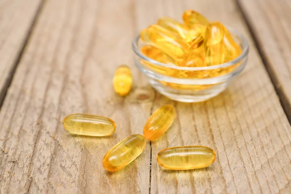 Fish oil capsules on wooden background, vitamin D supplement, selective focus