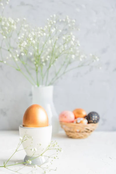 Close up of Golden egg in egg cup on the background of bouquet of gypsophila. Cozy easter still life