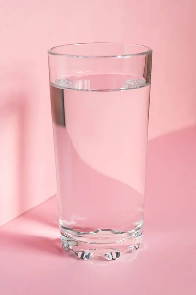 Close up of sparkling water in transparent high glass and sun glare on pink background.