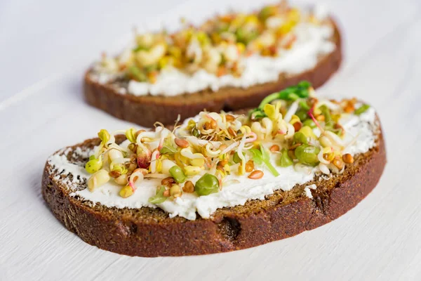 Healthy macrobiotic breakfast. Sandwich with cream cheese, peas microgreens and sprouted mung beans, walnut, sunflower and flax on wooden background. vegan, raw food diet