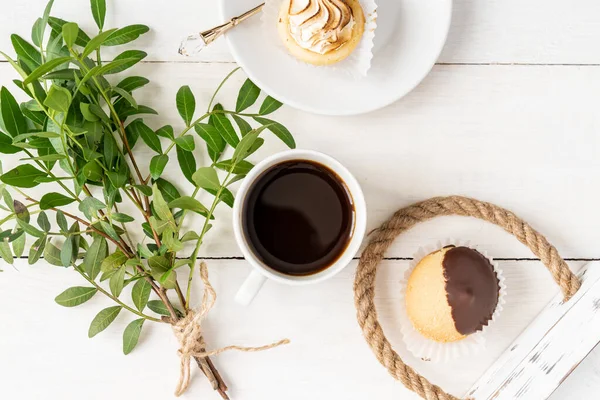 Morning cup of coffe, mini dessert and bunsh of green sprig leaves. Top view, light and airy flat lay.