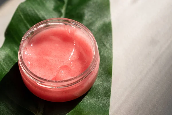 natural herbal cosmetic product for skin care. face and body jelly scrub in glass jar on green leaf.