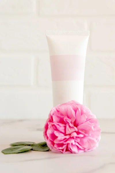 pink tube with rose face or body cream or scrub decorated with pink core flowers. Skin care concept. Unbranding mockup.