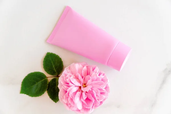 pink tube with rose face or body cream or scrub decorated with pink core flowers. Skin care concept. Unbranding mockup.