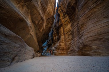 Ünlü Siq dar geçidinde yürüyen bir erkek turistin alçak açılı dikiz manzarası. Ürdün 'ün eski kenti Petra' ya giden yolda her iki taraftan da yükselen kumtaşı duvarlar. Dramatik ölçek duygusu.