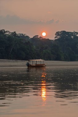 Tambopata Peru 'daki Madre de Dios Nehri' ne demirlemiş ahşap bir teknenin manzarası. Arka planda gün batımı parlıyor..