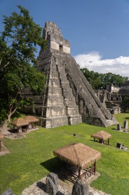 Büyük Jaguar Tapınağı 'nın dikey manzarası, ya da 1. Tapınak, çimenli Grand Plaza' nın ve Tikal Ulusal Parkı 'ndaki sazdan kulübelerin üzerinde yükseliyor..