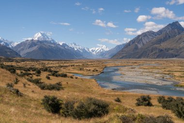 Örülmüş bir nehir manzarası ve altın vadi tabanı kar kaplı Aoraki Cook Dağı 'na ve Yeni Zelanda' nın güneyindeki Alplere doğru gidiyor..