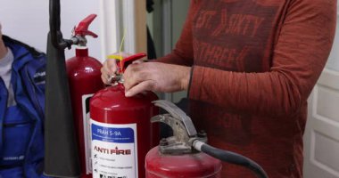 An instructional video demonstrating the correct use of a fire extinguisher, featuring clear, focused shots of hands performing the PASS technique (Pull, Aim, Squeeze, Sweep). 