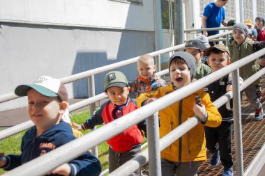 Moskova, Rusya - 12 Ağustos 2025: Bir grup genç, bir bakıcı ile birlikte, bir güvenlik korkuluğu ile dışarıda kuyrukta yürüyorlar. Anaokulu grup aktivitesi ve erken eğitim kavramı.