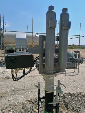 Mavi gökyüzünün altındaki inşaat alanında dikey silindirleri, vanaları ve kontrol kutuları olan endüstriyel gaz kurulumu enerji altyapısı ve mühendislik teknolojisini temsil ediyor..