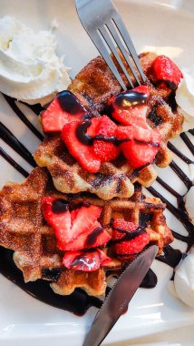 Çilekli waffle 'lar ve çatal ve bıçaklı bir tabakta çikolata serpiştirilmiş krema.