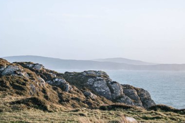 Ön planda kayalıklar, arka planda okyanus ve dağların görünen ana hatları, Koyun Başı, Batı Cork, İrlanda