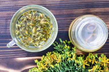 Şeffaf bir fincan St. John 's Wort şurubu ve taze sarı çiçekler..