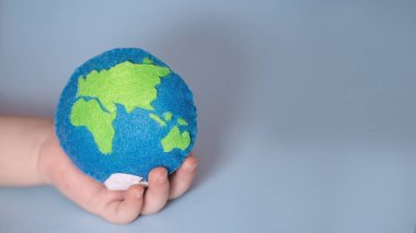 Küçük çocuk Dünya 'yı tutuyor. Gezegen şeklinde keçe şeklinde yüksüğü olan bir avuç çocuk. Çocuklarla ekolojiyi kurtarmak. Cosept Dünya Günü. Dünya Okyanus Günü, su tasarrufu kampanyası..