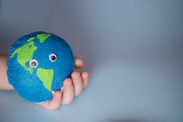 small child holds Earth. palm of child with thimble of felt in form of planet. Saving Ecology with children. Cosept Earth Day.World ocean day, saving water campaign.