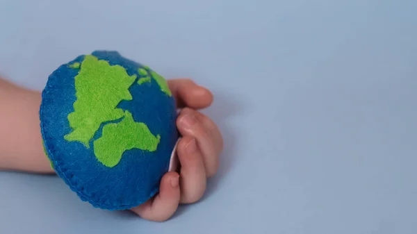 small child holds Earth. palm of child with thimble of felt in form of planet. Saving Ecology with children. Cosept Earth Day.World ocean day, saving water campaign.