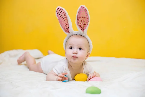 Happy easter funny funny baby with ears hare lies on crib and collects Easter eggs. egg hunt concept