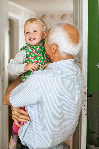 gray-haired grandfather with a blond-haired girl in arms. grandfather\'s and granddaughter\'s head is close by. Closeup photo of funny two people old grandpa little granddaughter