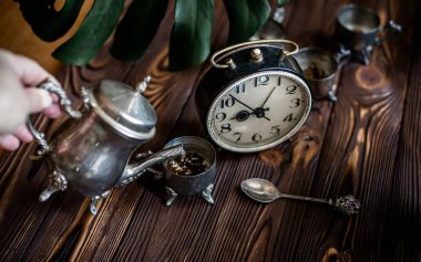 Kahvaltıda. Eski bir kahve demliğinden el yapımı kahve. Eski bir çalar saatin yanında gümüş bir kupa. Zaman doldu. Çok az zaman. Güneşin doğuşuyla aydınlanan bir masada gümüş mahsullü dama. İş günü için hazırlanılıyor.