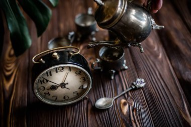 Kahvaltıda. Eski bir kahve demliğinden el yapımı kahve. Eski bir çalar saatin yanında gümüş bir kupa. Zaman doldu. Çok az zaman. Güneşin doğuşuyla aydınlanan bir masada gümüş mahsullü dama. İş günü için hazırlanılıyor.