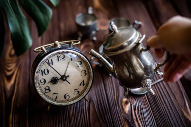 Kahvaltıda. Eski bir kahve demliğinden el yapımı kahve. Eski bir çalar saatin yanında gümüş bir kupa. Zaman doldu. Çok az zaman. Güneşin doğuşuyla aydınlanan bir masada gümüş mahsullü dama. İş günü için hazırlanılıyor.